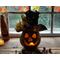 This shows the fall pumpkin gourd lit up with a battery-operated candle. Briar the pumpkin sits in front of a fall window display. 